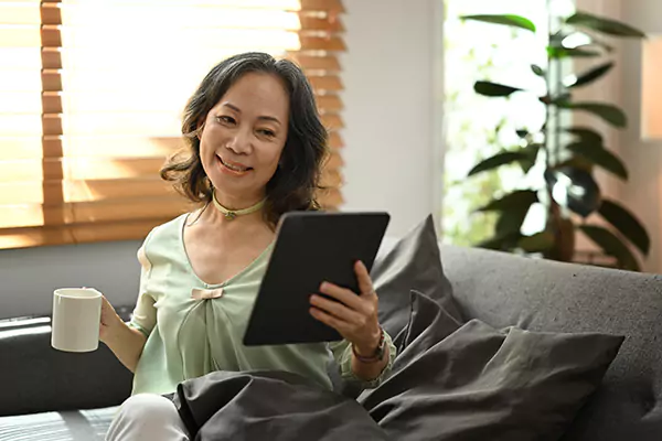 Senhora sorrindo, segurando tablet e xícara de café